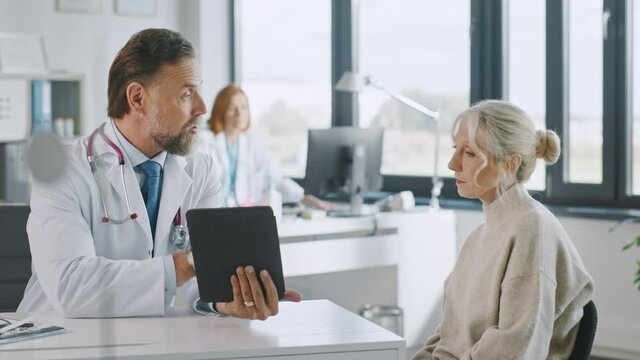 Friendly and Cheerful Family Doctor is Reading Medical History of Senior Female Patient During Consultation in a Health Clinic