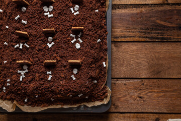 Kuchen als Friedhof mit Gräbern und Skeletten aus Schokokrümel, Creme und Banane auf Tisch aus Holz und dahinter Spinnweben