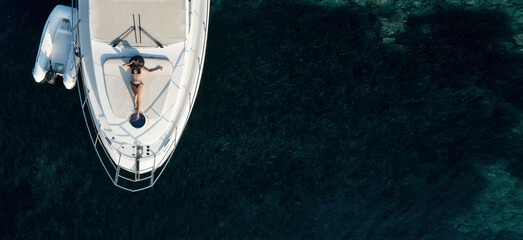 Aerial view at beautiful young woman relaxing on a private yacht deck in the sea. - obrazy, fototapety, plakaty