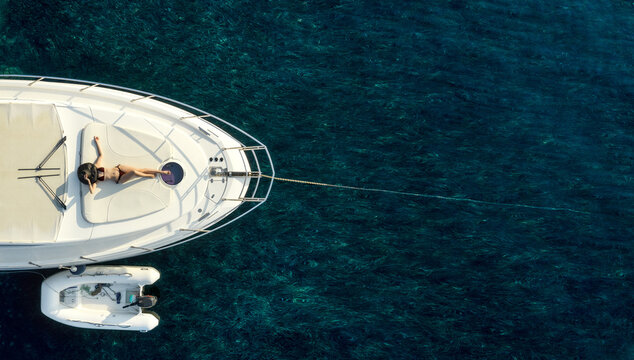 Directly above view at white luxury yacht with woman in swimsuit and hat laying on. Copy space