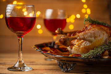 The Thanksgiving traditional turkey on the plate isolated on wooden background. The glasses with red wine are on the table. Yellow lights for festive atmosphere.