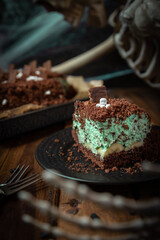 Kuchen als Friedhof mit Gräbern und Skeletten aus Schokokrümel, Creme und Banane auf Tisch aus Holz und dahinter Spinnweben