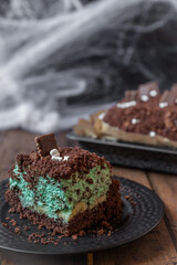 Kuchen als Friedhof mit Gräbern und Skeletten aus Schokokrümel, Creme und Banane auf Tisch aus Holz und dahinter Spinnweben