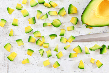 Yellow green avocado pulp cut to small pieces on white stone like desk, knife blade near, view from above