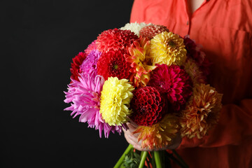 Woman with bouquet of beautiful dahlia flowers on black background, closeup