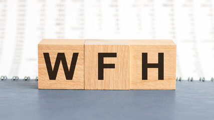 concept image a wooden block and word WFH - Work From Home - with shadow selective focus a row of blocks is located on a notepad. Background of columns of numbers, front view.