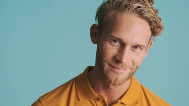Handsome blond bearded man smiling and winking on camera over colorful background
