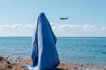 Person wearing a ghost costume made from blue sheet and standing on the beach