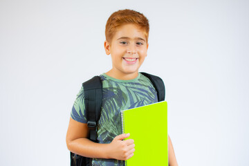 Happy smiling red-haired boy with thumb up is going to school. Child with school bag and book