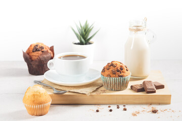 A variety of muffins with a cup of milk chocolate on a wooden board on a white background.