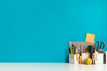Creative desk with a blank picture frame or poster, desk objects, office supplies, books, and plant on a blue background.	
