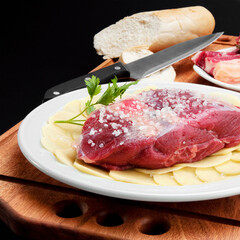 Close-up of a raw steak on a bed of sliced potatoes marinated with rock salt