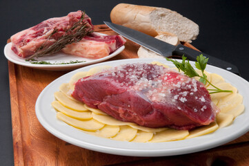 Close-up of a raw steak on a bed of sliced potatoes marinated with rock salt