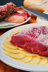Close-up of a raw steak on a bed of sliced potatoes marinated with rock salt