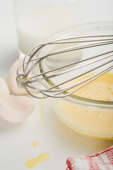 Egg yolk in a bowl with wire whisk and a milk bottle
