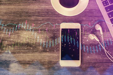 Double exposure of forex chart hologram over desktop with phone. Top view. Mobile trade platform...