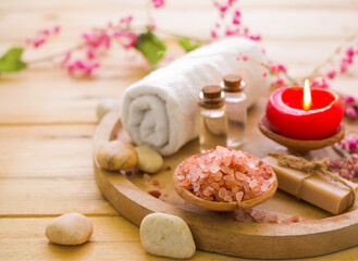 Obraz na płótnie Canvas Himalayan salt and coconut oil, massage oil with , soap, candle on wood background with pink flower petals on white towel for luxury hotel or professional massage. aroma therapy spa set concept.