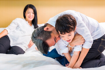 Fototapeta na wymiar Asian Mother, father and their cute son resting together on bed in hotel room.