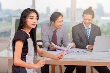 Beautiful young asian woman in office and confident expression as other workers hold a meeting in background.