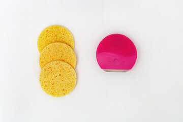 Electric silicone face brush and facial cleanser sponges on white concrete background. Accessories...