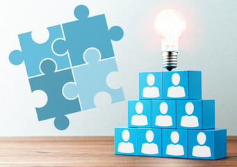 Business teamwork and solution. Puzzle pieces illustrations, lightbulb and stacked blue blocks with person icons on wood table.