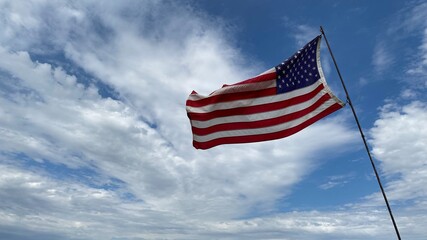 Waving American flag against blue sky and clouds.
