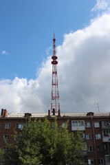Fototapeta na wymiar a high TV tower in the city above an apartment building emits radio signals