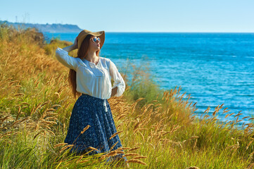 Young beautiful red-haired woman in a dress and a wide-brimmed hat in nature