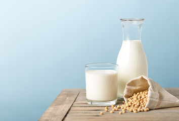 Glass of soy milk with bottle and soybeans on wooden table.