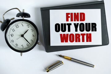 On the table there is a clock, a pen, a notebook and a card on which the text is written - FIND OUT YOUR WORTH