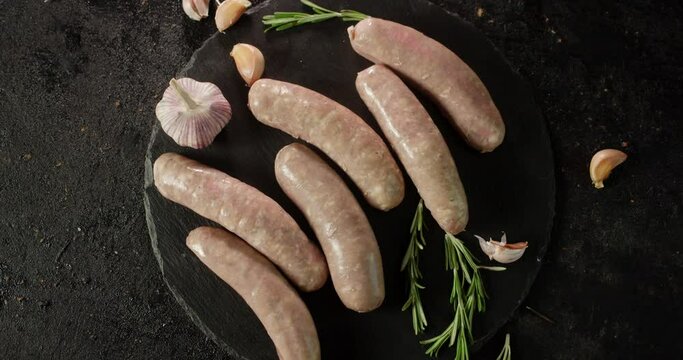 Raw sausages with rosemary and garlic rotate on a table.