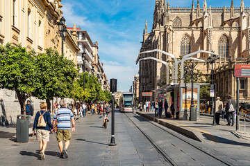 Fototapeta premium Seville, Spain. October 15th, 2020. Tram line stop at Avenida de la Constitucion with Cathedral in the background. Many people on the street.
