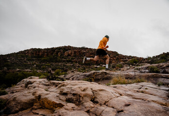 Wide angle young male athlete running up wet mountain rock track muscular legs cold cloudy weather