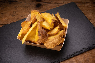 carton foil of fries with peel on slate tray over wooden table