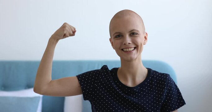Head shot of enthusiastic bald girl smile looks at camera demonstrate biceps arm muscle, patient make effort stay alive struggle against oncology disease, shows strength of mind, fights cancer concept