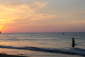 Naklejka na ściany i meble Peschici, Foggia - Sunset on a beach with peorle swimming in the sea