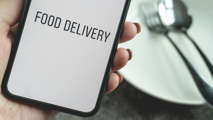 Women hand holding smartphone for food delivery online with plate and cutlery blur background. 