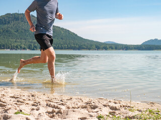 Man is running in lake and  splashing water around him. Sportsman costumes run in pond, happy man feet splash water