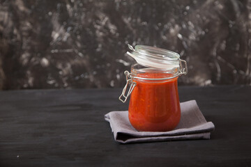 Sharissa spicy podpava in a glass jar stands on a linen napkin on a black background. Traditional national cuisine. Copy spaes.
