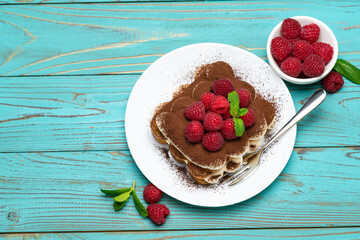portion of Classic tiramisu dessert with raspberries on blue wooden background