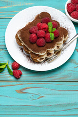 portion of Classic tiramisu dessert with raspberries on blue wooden background
