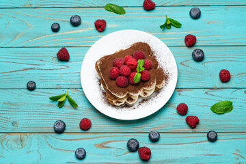 Naklejka na ściany i meble portion of Classic tiramisu dessert with raspberries and blueberries on blue wooden background