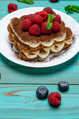 portion of Classic tiramisu dessert with raspberries and blueberries on blue wooden background
