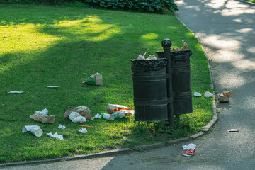 Scattered garbage around the trash can in the park. The birds took everything out of the trash bin.