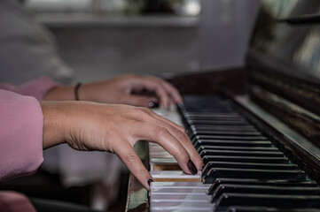 Fototapeta premium Hands of a girl on piano keyboard. Teenage girl learns to play the piano.