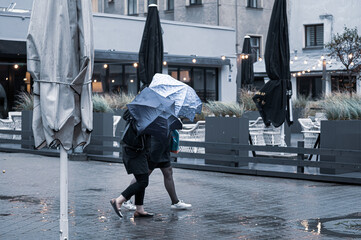 Girls take shelter with umbrellas from light rain and strong wind outside in bad weather.