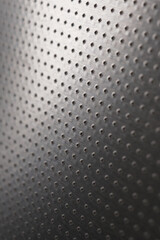 Dark vertical industrial wallpaper or background. Perforated aluminum surface with many holes. Abstract tech or electronic backdrop. Macro