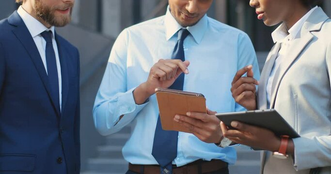 Multi ethnic males and female white-collars workers standing outdoors at street and watching something on tablet device. Mixed-races men and woman using tablets gadgets. Coworking. Brainstorming.