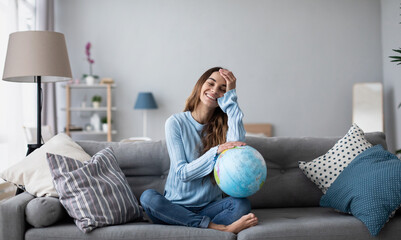 Beautiful woman dreaming about vacation with a globe model sitting on the couch.
