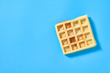 One vanilla belgian waffle on blue background. Top view